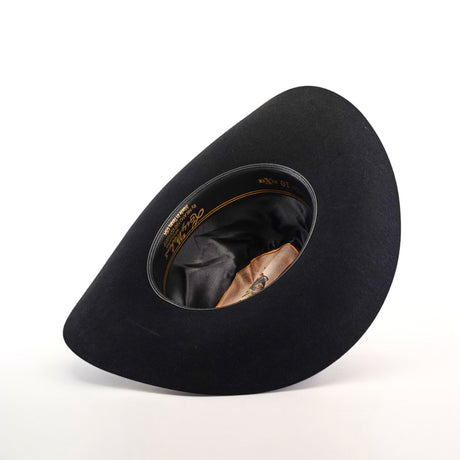 The 10X Jerarca Black, a handcrafted cowboy hat, is displayed upside down to reveal its smooth black lining and brown sweatband. This elegant western hat features a classic wide brim and high crown, capturing the timelessness of traditional fur felt headwear.