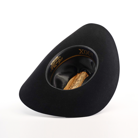 The 100X Independecia Black is a black, wide-brimmed hat turned upside down, showcasing its satin lining and leather headband. This epitome of western headwear features elegant gold detailing inside, including the distinguished Larry Mahan 100X.