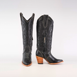 The Linda Studs Tall Shaft Black - J Toe boots from the Platinum Collection are luxury handcrafted cowboy boots with intricate patterns, decorative studs, a tall shaft, side zipper, and stacked wooden heels. One boot is upright while the other is angled to highlight its artistry.