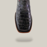 A close-up of the Exotic American Alligator Belly - Black - Square Toe cowboy boot highlights its exquisite Western craftsmanship against a plain gray background, showcasing the quality sole and heel and emphasizing its elegant design.