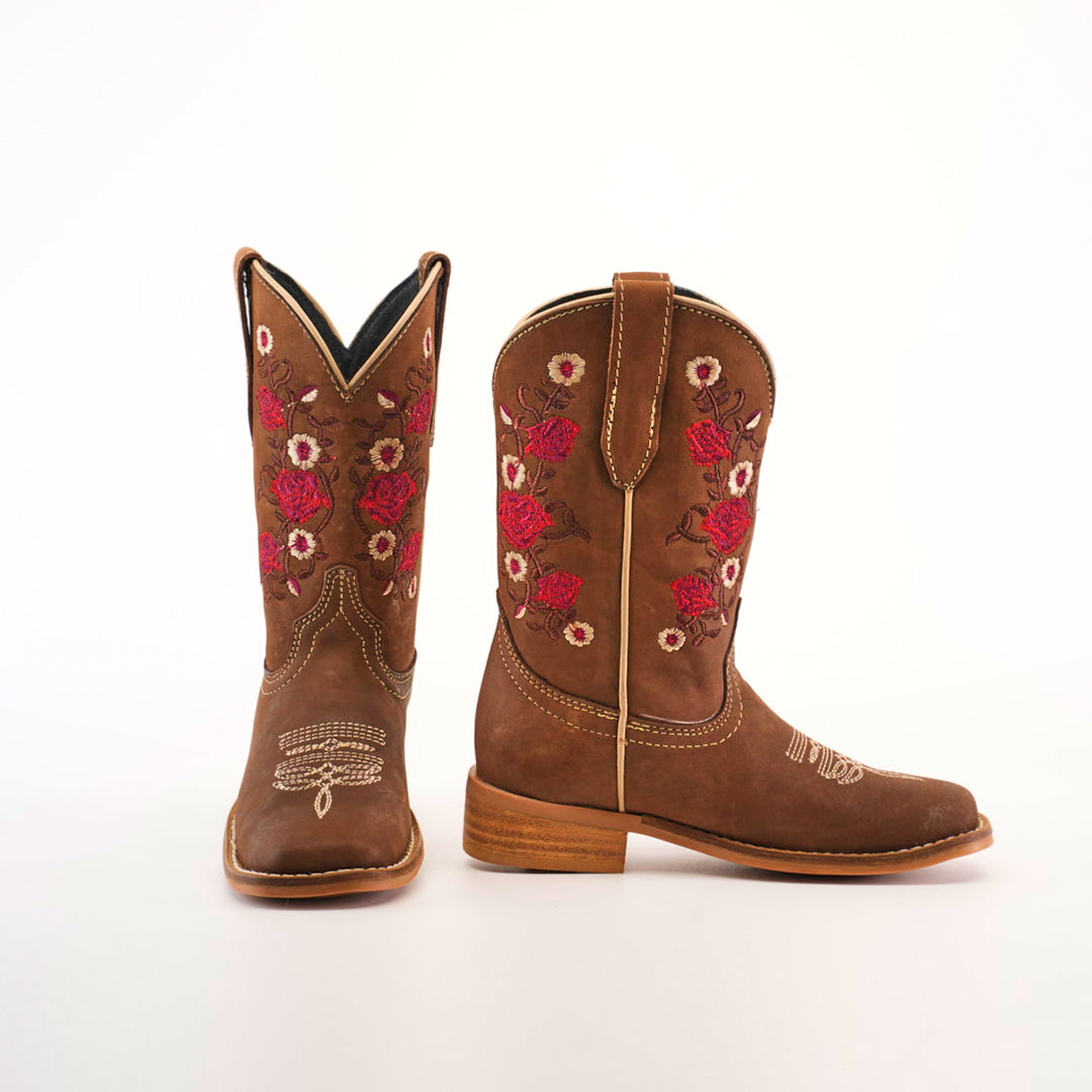 The Mia Copper Suede - Square Toe cowboy boots boast premium leather craftsmanship with intricate pink and white floral embroidery on brown shafts, featuring a wooden heel and decorative white stitching on the toes against a simple white backdrop.