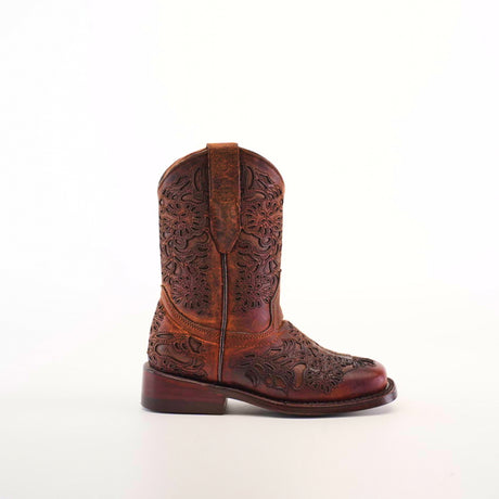 The Yennis Brick Square Toe, a girls cowboy boot, showcases intricate floral embossing. Crafted from premium brown leather, it stands upright against a white background with a low heel and convenient side pull straps for easy wear.