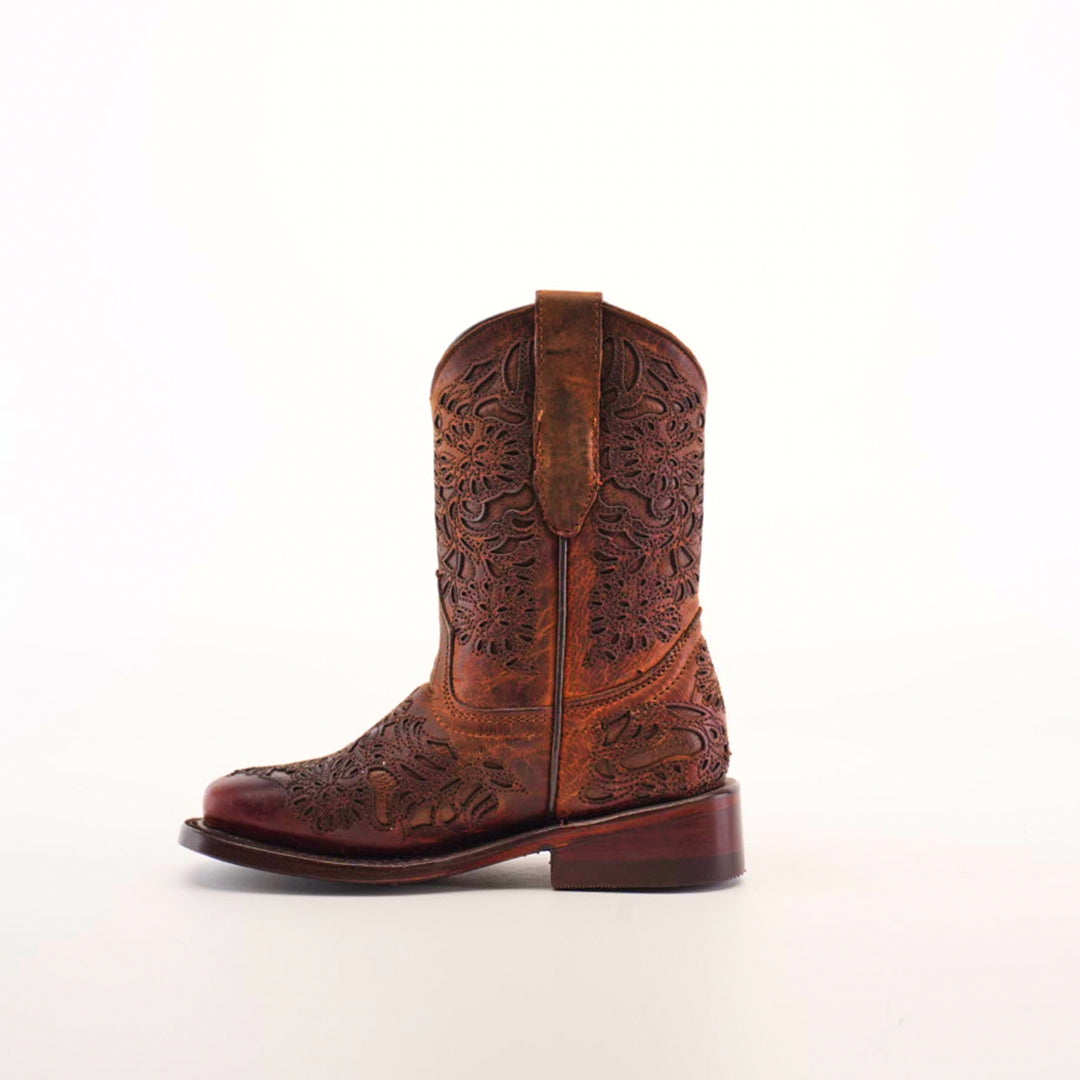 The Yennis Brick Square Toe boot showcases a brown, premium leather design with intricate floral embroidery on a plain white background. It features a short heel and a pull tab at the top, seamlessly combining style with quality craftsmanship.