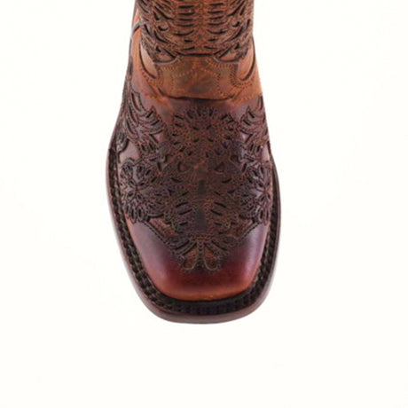 A close-up of the Yennis Brick Square Toe cowboy boot, featuring intricate embossed floral patterns on brown, handmade leather. The premium material has a worn appearance, highlighting its rich texture and natural color variations.