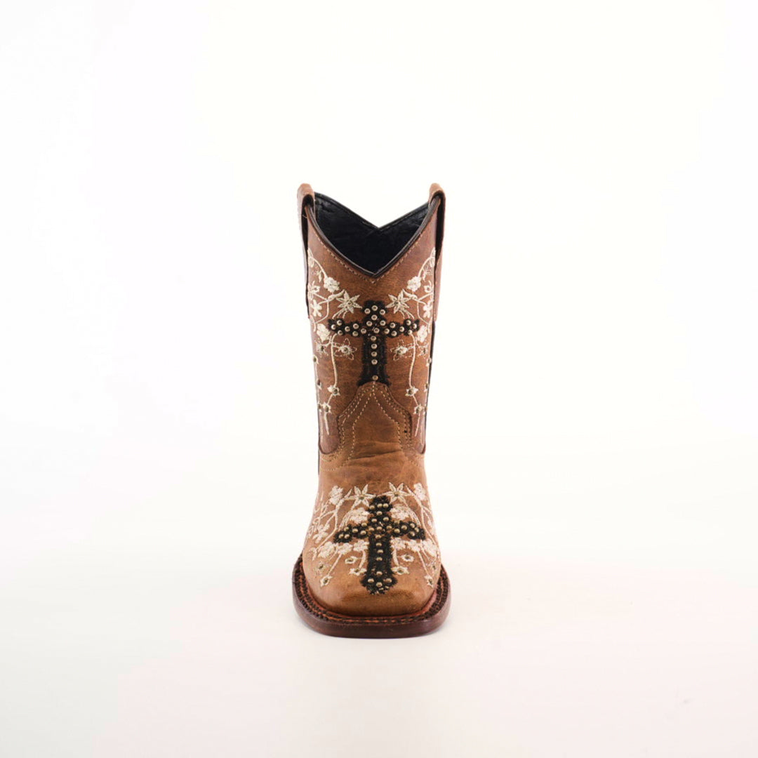 The Margacruz Studs Orix - Square Toe, a single brown cowboy boot, handcrafted from premium leather, features ornamental stitching with floral and cross designs in white and black. It stands upright against a plain white background.