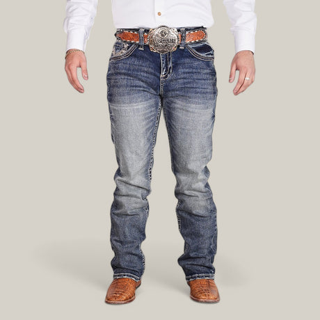 A person in a white long-sleeve shirt and Western Blue Straight Fit Embroidered Jeans - W436 stands facing forward. Brown leather boots and a wide, ornate belt with a large detailed buckle enhance their style against the plain light gray background.