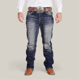 A person wearing Western Blue Straight Fit Embroidered Jeans - W433, a white shirt, and a large belt with an ornate buckle. They sport brown textured boots against a plain, neutral background.