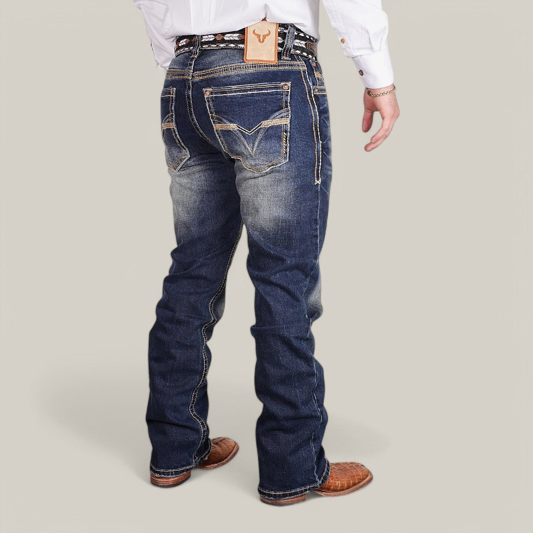 A person stands with their back turned, wearing Western Blue Straight Fit Embroidered Jeans - W433, a white shirt, and cowboy boots. The jeans feature decorative stitching and a leather patch at the waistline, all against a plain gray background.