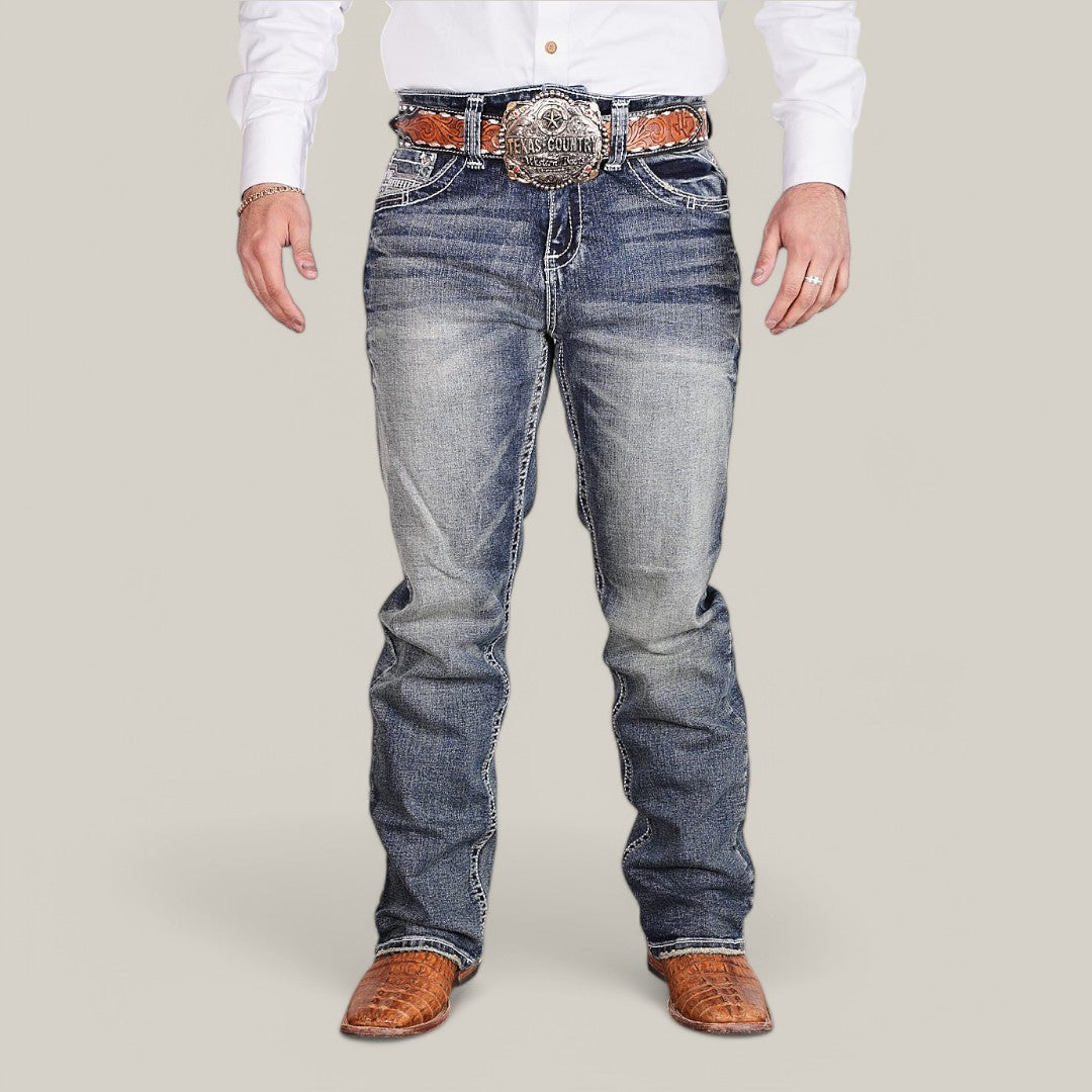 A man wears Western Blue Straight Fit Embroidered Jeans - W431 with white stitching, a large belt buckle, a brown leather belt, and brown crocodile-patterned boots. His white shirt enhances his rugged style, showing only his torso and legs against a neutral backdrop.