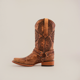 The Siberia Fawn - Biker Toe is a single brown leather cowboy boot made from premium cowhide. It features intricate floral patterns, a decorative ankle strap, a stacked wooden heel, and is set against a plain white background.