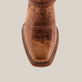 Close-up of the Siberia Fawn - Biker Toe boot, showcasing a brown, square-toed design with intricate toe stitching. Made from premium cowhide, its rustic leather features detailed embroidery and white edge stitching.