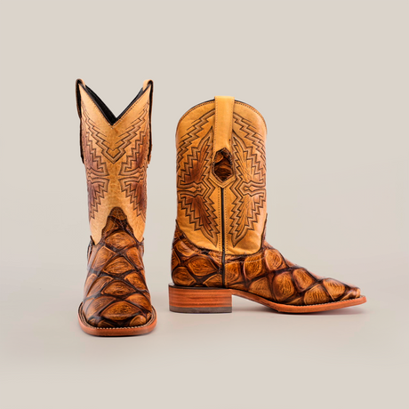 The Big Bass Pirarucu Print Orix Square Toe cowboy boots showcase a premium cowhide leather build with intricately designed square toes. They feature a textured brown pattern on the foot and ornate geometric stitching on the tan shaft, set against a plain background.