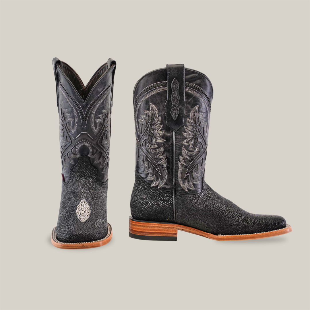 The King Stingray Print Black boots boast intricate embroidery on premium cowhide leather. These handcrafted boots have square toes and wooden soles, with one boot facing forward and the other turned to the side, all set against a plain white background.