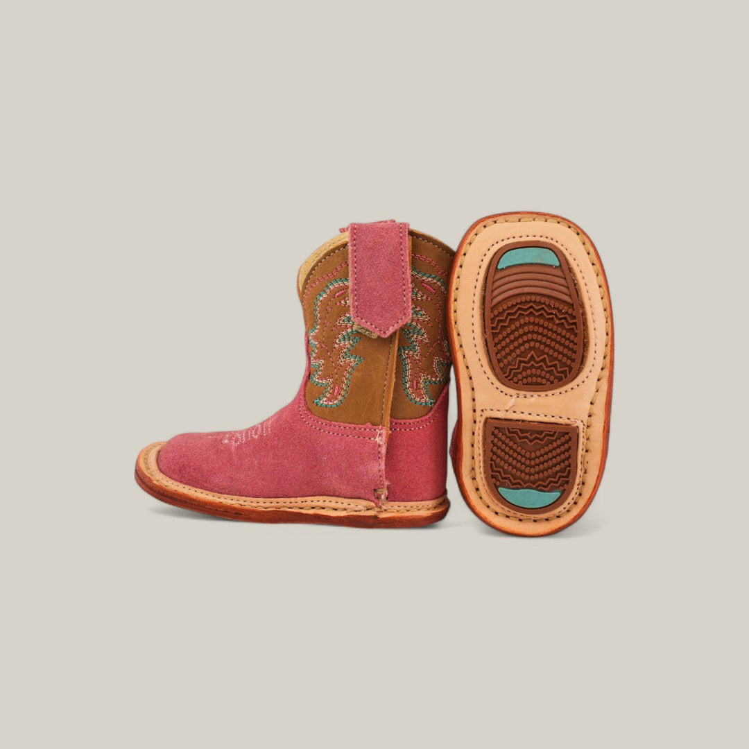 The Harper boots feature two small pink suede cowboy boots: one upright, one showing the sole. They include brown accents, decorative stitching, light brown textured grip soles with turquoise details, and a stylish square toe design.