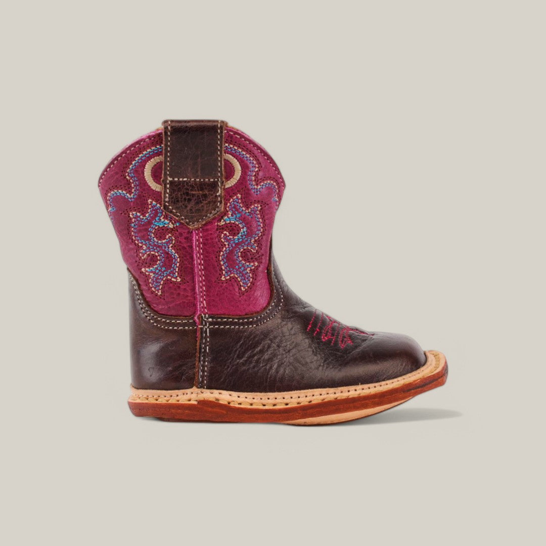 Introducing the Emma Baby Boot, featuring a charming square toe. This childs cowboy boot has a dark brown foot, a vibrant pink upper adorned with blue and purple embroidery, and is finished with a tan sole and two pull straps for easy wear.