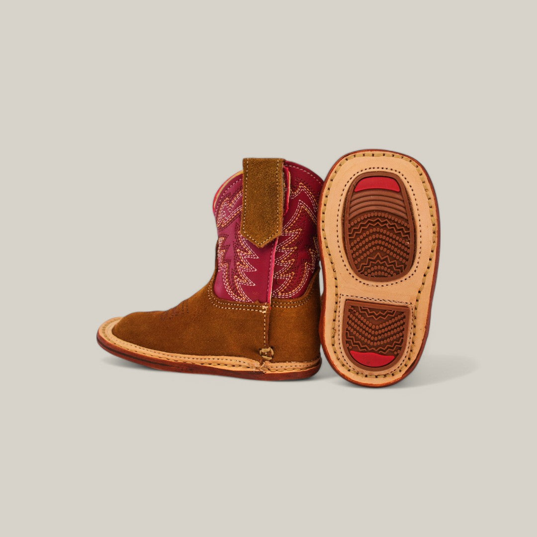 A pair of Sommer - Camel Red Shaft - Square Toe boots, made from premium materials, features decorative stitching. One boot stands upright highlighting the striking camel red shaft, while the other lays on its side to display a beige and red sole with textured grips against a plain background.