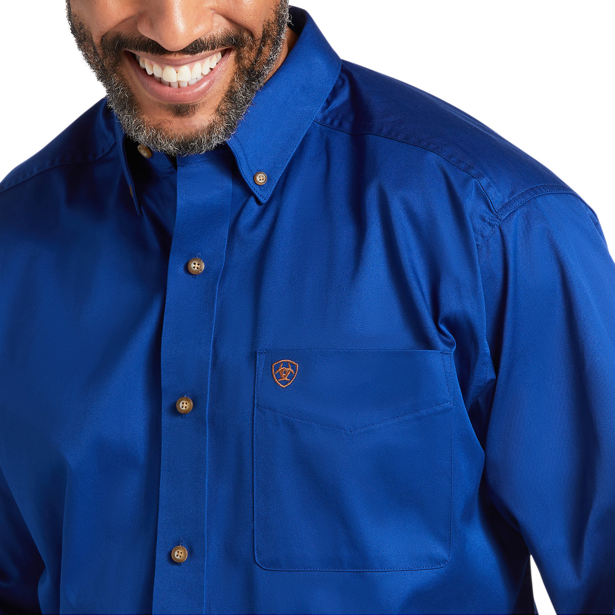 A person smiling in a Solid Twill Classic Fit Shirt Blue - 10006660, made of 100% cotton twill, with brown buttons and a small emblem on the pocket. The smart collar adds to its charm. Image highlights the upper chest and part of the face.