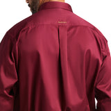 A person is wearing a Solid Twill Classic Fit Shirt in Burgundy (product 10012635), with ARIAT embroidered below the collar. The shiny fabric looks smooth as they partially face away, showing their head.