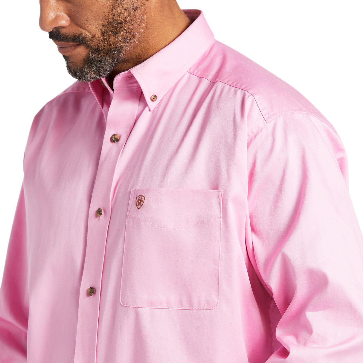 A man wears the Solid Twill Classic Fit Shirt Pink (10016692), featuring a chest pocket, embroidered logo, collar, and brown buttons. He faces slightly sideways, highlighting its timeless style.