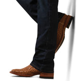 A person leans against a white wall in brown ostrich leather western boots with quill marks and a stacked heel, wearing M4 Relaxed Hansen Boot Cut Jean - Blackstone, offering a casual, stylish look.