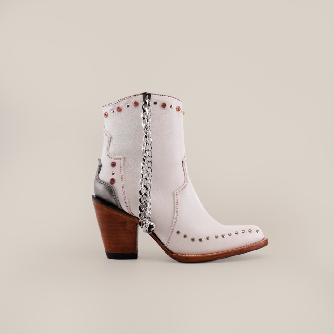 Explore the Milan Chains Bootie Frost White - J Toe, a white leather ankle boot from the Platinum Collection with decorative studs and a silver chain. It features a medium wooden heel, dark sole, and is shown from the side against a plain background