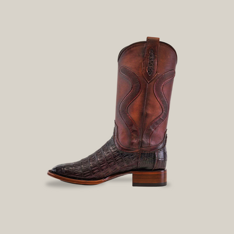 The Exotic Caiman Belly Tail - Diamond - Tabaco - Square Toe cowboy boot, part of the Platinum Collection, showcases intricate stitching and an embossed pattern. It features a dark wooden heel, embodying Western fashion against a plain beige background.