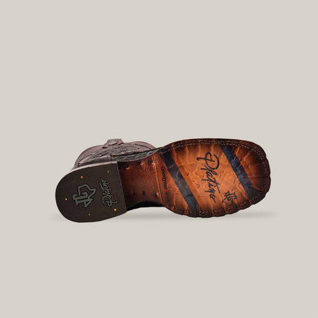 The image shows the outsole of an Exotic Caiman Belly Tail - Diamond cowboy boot in Tabaco, featuring a classic square toe style. The Goodyear welt construction includes visible stitching and Justin branding on a rugged-textured heel, all set against a plain beige background.