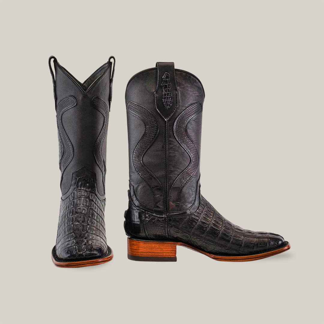 Meet the Exotic Caiman Tail - Diamond Black boots with a square toe, featuring black alligator texture and detailed stitching. One boot stands tall showing its front, the other its side profile, showcasing expert craftsmanship with brown leather soles.