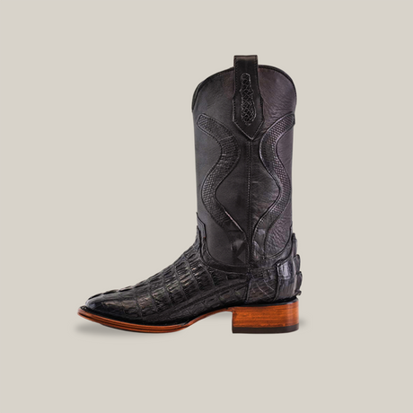 Discover the Exotic Caiman Tail - Diamond Black cowboy boot with a square toe and intricate textures, evoking caiman tail patterns, complete with a wooden heel against a plain background.