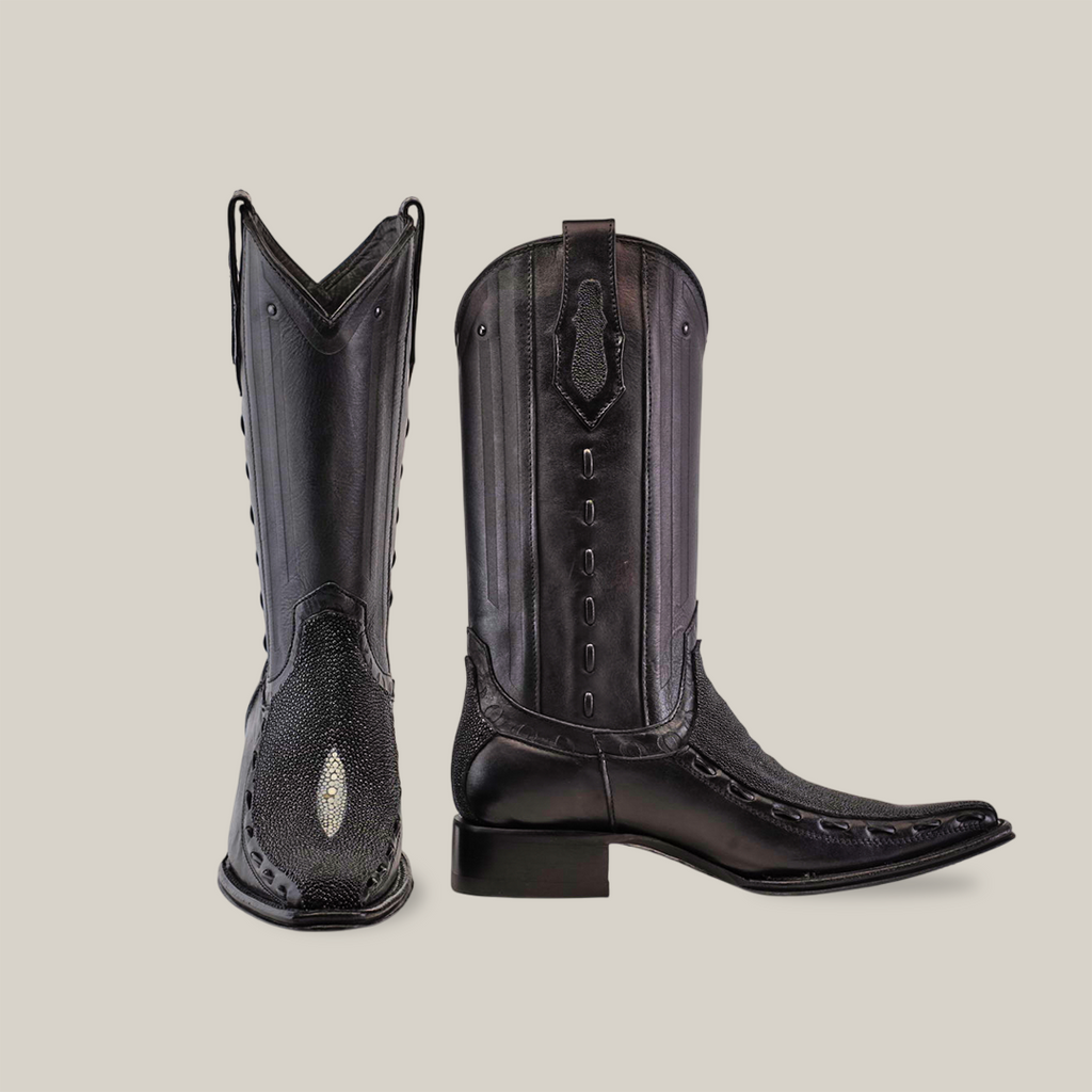 A pair of Exotic Stingray - Platinum - Black - Versy Toe boots, showcasing elegant intricate stitching and decorative tooling. One boot stands upright, the other lies down to display their unique design and shine against a plain white background.