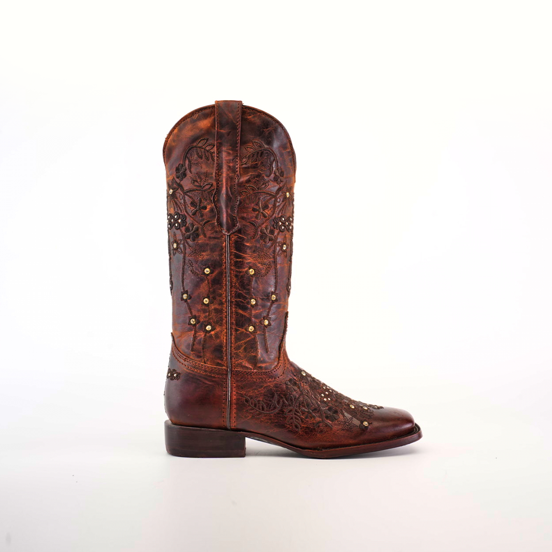 A single Marga Cruz Brick Mid Shaft boot, featuring intricate floral embroidery and gold studs, stands against a white background. Crafted from premium leather, its weathered look highlights the artistry of handcrafted boots.