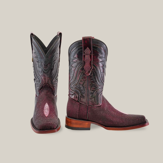 The Exotic Stingray - Wine - Rodeo Toe boots are crafted from exquisite dark red stingray leather with intricate stitching and scroll designs. They feature a pointed toe, one boot facing forward and the other showcasing the side design and wooden heel—truly luxury footwear at its finest.