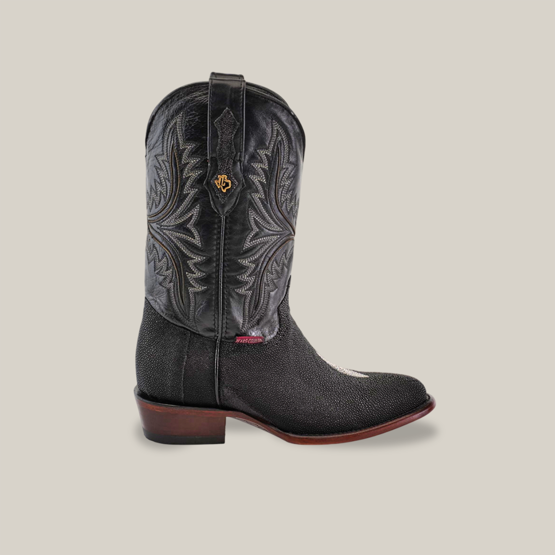 The Exotic Stingray - Black - Round Toe boot features intricate shaft stitching, a logo emblem, and a textured vamp. It showcases a round toe and dark brown heel, creating an impactful look against a neutral background.