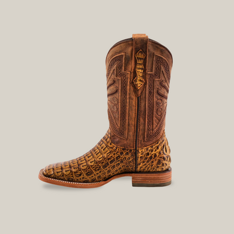 The Exotic Caiman Horn Back - Antique - Square Toe boot showcases intricate patterns and a textured, reptile-like finish. Crafted by skilled artisans, this brown boot features a flat heel and elaborate stitching on the shaft, all set on a plain background.