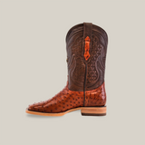 An Exotic Full Quilt Ostrich - Brandy - Square Toe boot, capturing the cowboy spirit, stands upright against a plain backdrop. This handcrafted brown leather boot boasts a smooth lower section with intricate upper shaft patterns and a sturdy heel and sole.