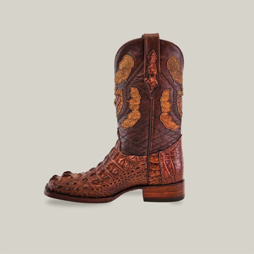 The Exotic American Alligator Head boots in brown feature intricate patterns, a textured surface, decorative lighter shades, a square toe, and a low wooden heel against a plain beige background.