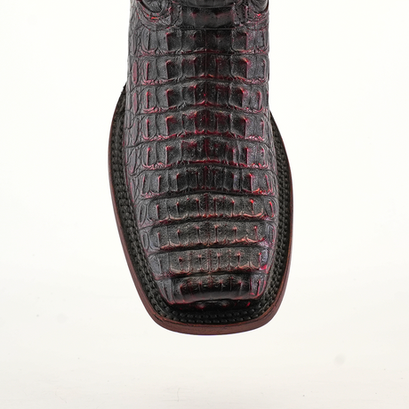 A close-up of the Exotic Caiman Hornback - Black Cherry boot showcases its black and red crocodile pattern with a square toe, crafted from genuine caiman leather. White stitching around the sole highlights expert craftsmanship against a pristine white background.