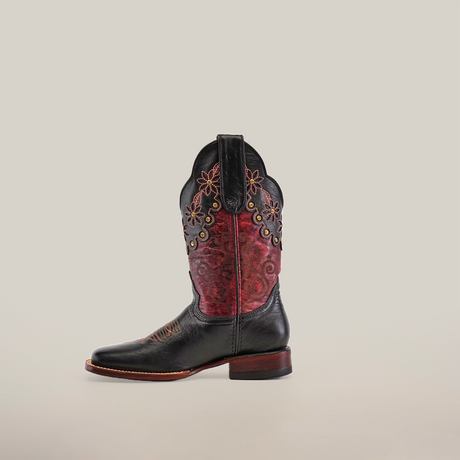 The Grecas Black - Short Shaft - Square Toe boot features floral embroidery on a red and black upper, black leather at the foot, a brown wooden heel, and a pointed toe, showcasing its handcrafted artistry against a plain white background.