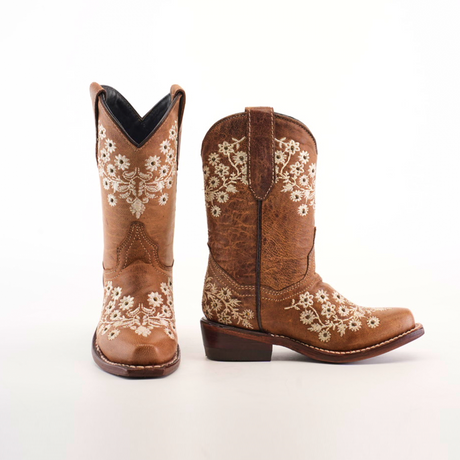 The Abril Studs Orix Snip Toe boots are brown leather cowboy boots with intricate white floral embroidery on the sides and front, featuring a stylish snip toe and stacked heel, showcased against a plain white background.