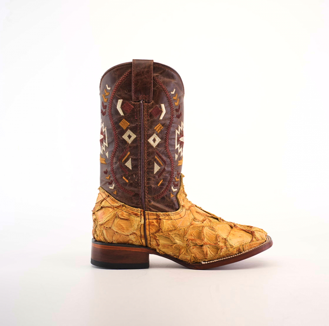 The Exotic Pirarucu Fish Patchwork Honey Square Toe boot features a yellow-textured lower section mimicking fish scales and a dark brown leather upper with geometric white and brown patterns. Its presented standing against a clean white background.