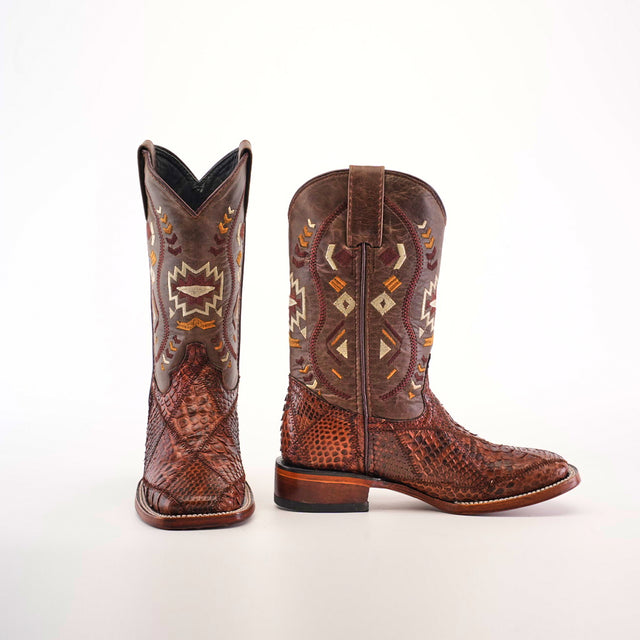 A pair of Exotic Python Patchwork Chocolate Square Toe boots, featuring intricate geometric designs in cream and tan, crafted from python leather with a textured look, wooden sole, and curved top. One stands upright while the other is on its side.