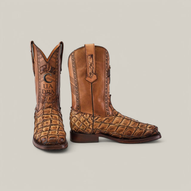 The Asturias Honey Fish Pirarucu Laser & Woven - Square Toe (CU658) cowboy boots are displayed on a plain background, one standing upright and the other leaning to reveal intricate stitching and a logo-embossed, laser-engraved shaft.