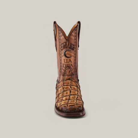 The Asturias Honey Fish Pirarucu Laser & Woven boot CU658 features a square toe, embossed brown leather, and laser-engraved shaft with CUADRA prominently displayed. Set against a plain background, its unique texture and decorative design stand out.