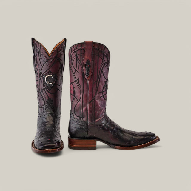 The Blackcherry Ostrich Laser & Embroidery Square Toe CU786 boots feature a tall design with intricate purple and black leather patterns, one upright and the other on its side, revealing laser-engraved details on the sole and heel against a plain light background.