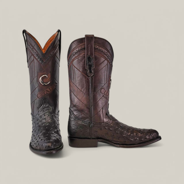 A pair of black ostrich boots with laser-cut and woven designs from Cuadra. These elegant CU554 boots feature round toes, shown side by side, one facing front and the other from the side.