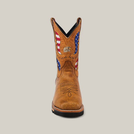 The Taurus Honey Soft Toe - E6189 is a single cowboy boot made from durable tan leather, adorned with American flag patterns and an eagle on the upper shaft. It stands out against a plain, light background, symbolizing both style and resilience.