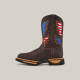 The Taurus Moka Soft Toe - E6189 is a single brown cowboy boot with decorative American flag patches in blue, white, and red on the shaft. It features a rugged sole with detailed stitching for durability against a plain light gray background.