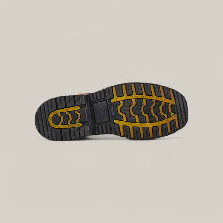 The image highlights the durable sole of a black Crazy Honey Composite Toe - E6048 boot, featuring yellow-accented patterns. Its wavy and parallel line tread design ensures grip, perfect for waterproof boots. The backdrop is a plain light beige.