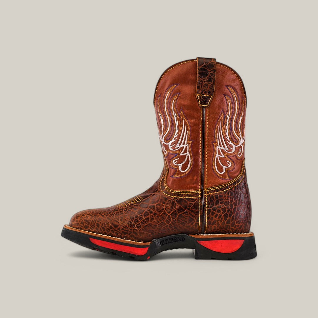 The Jurasic Honey Soft Toe - E6080 is a brown cowboy boot with intricate white stitching and red-accented black sole. It features a textured pattern for durability, an easy pull-on loop, and is set against a neutral backdrop, making it perfect for any rugged adventure.