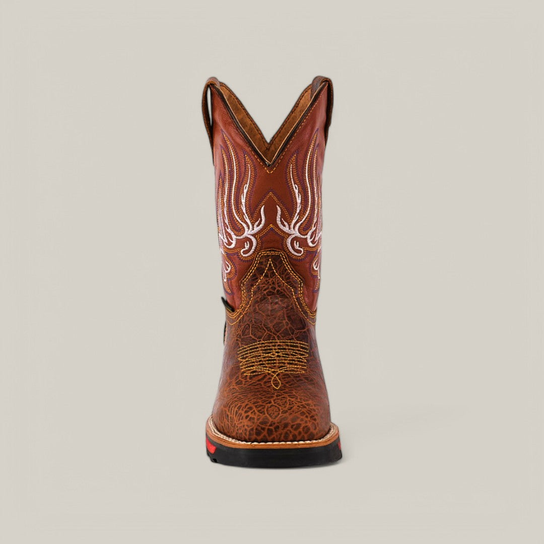 Front view of the Jurasic Honey Soft Toe - E6080 cowboy boot shows a brown hue with intricate white stitching and patterns on the shaft. It features a slightly rounded toe, low heel, rugged texture, and red accent on the soles edge, known for durability.